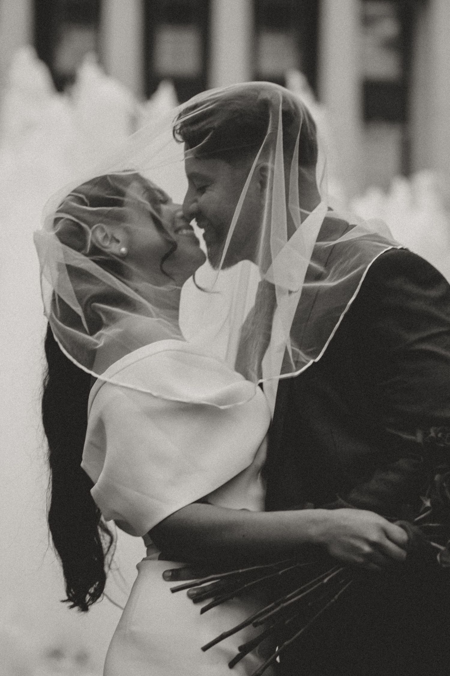 A romantic black and white wedding photo showing a tender kiss between newlyweds with the bride's veil flowing.