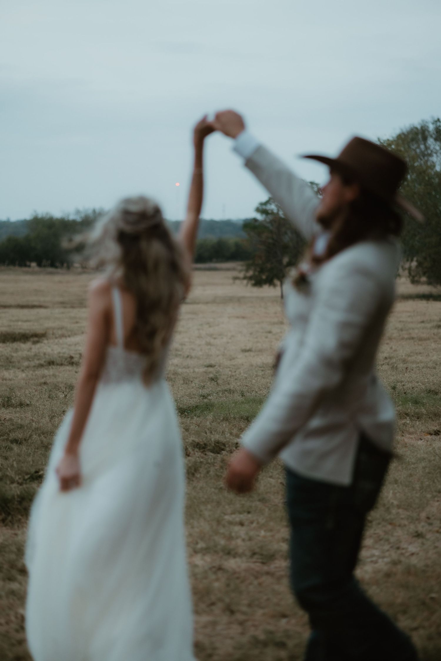 A couple in wedding attire dances and spins together in a blurry artistic sequence on a rustic outdoor field.