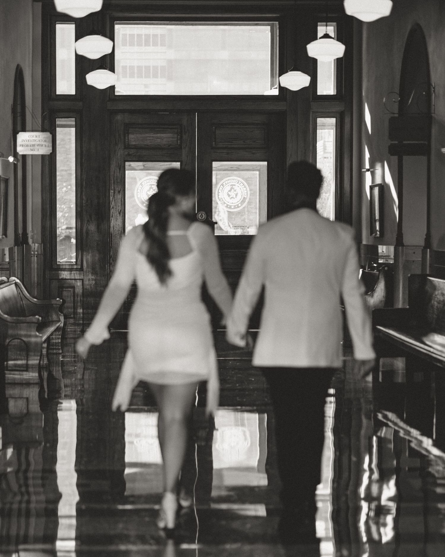 Black and white photograph of silhouettes walking across a brightly lit corridor interior with dramatic lighting.