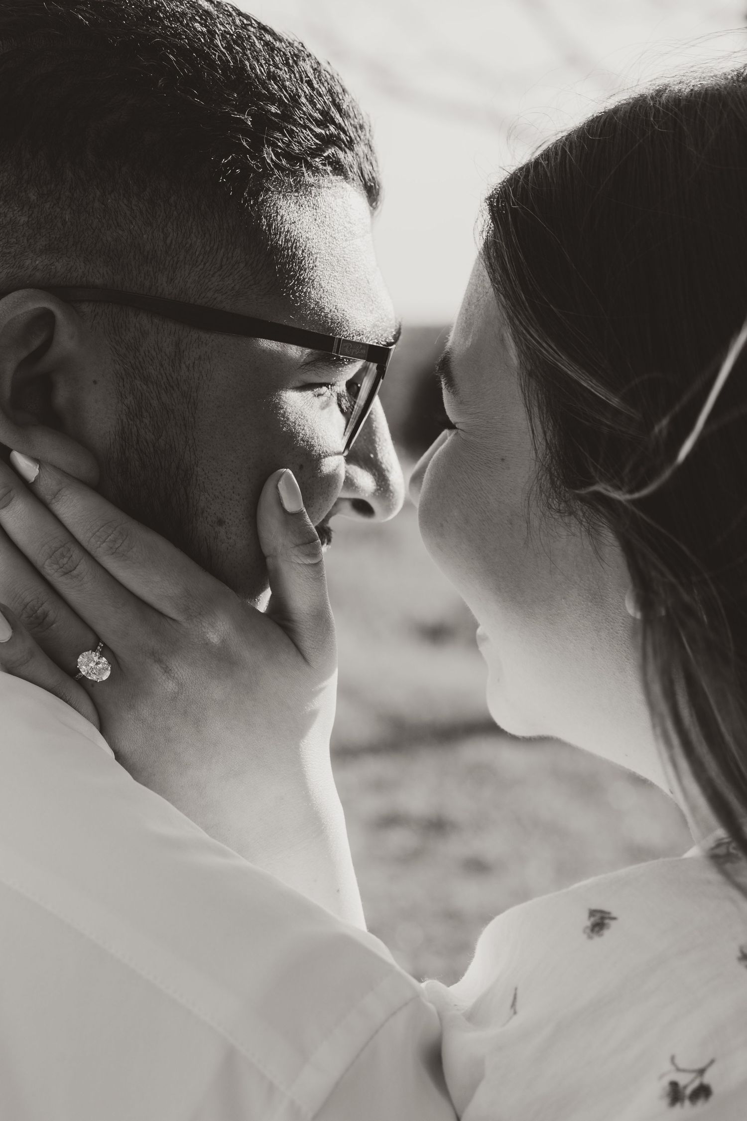 An intimate black and white close-up photo of a couple sharing a tender kiss outdoors.