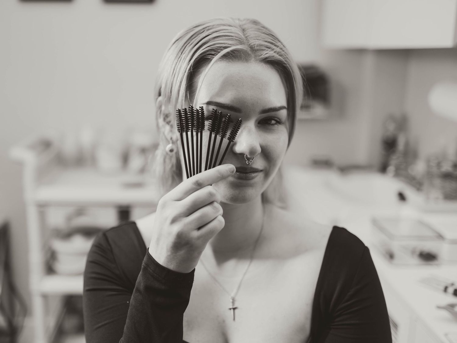 Black and white photograph of someone playfully holding a set of makeup brushes in front of face.