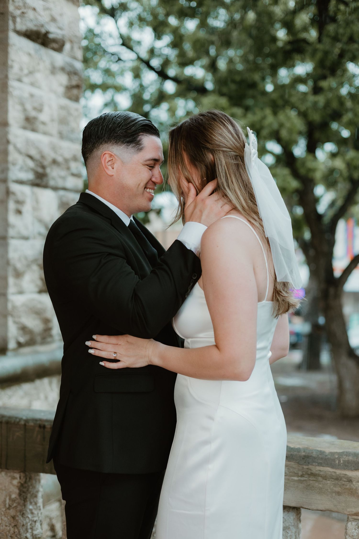 A couple shares an intimate moment outdoors against a stone wall backdrop during their wedding ceremony.