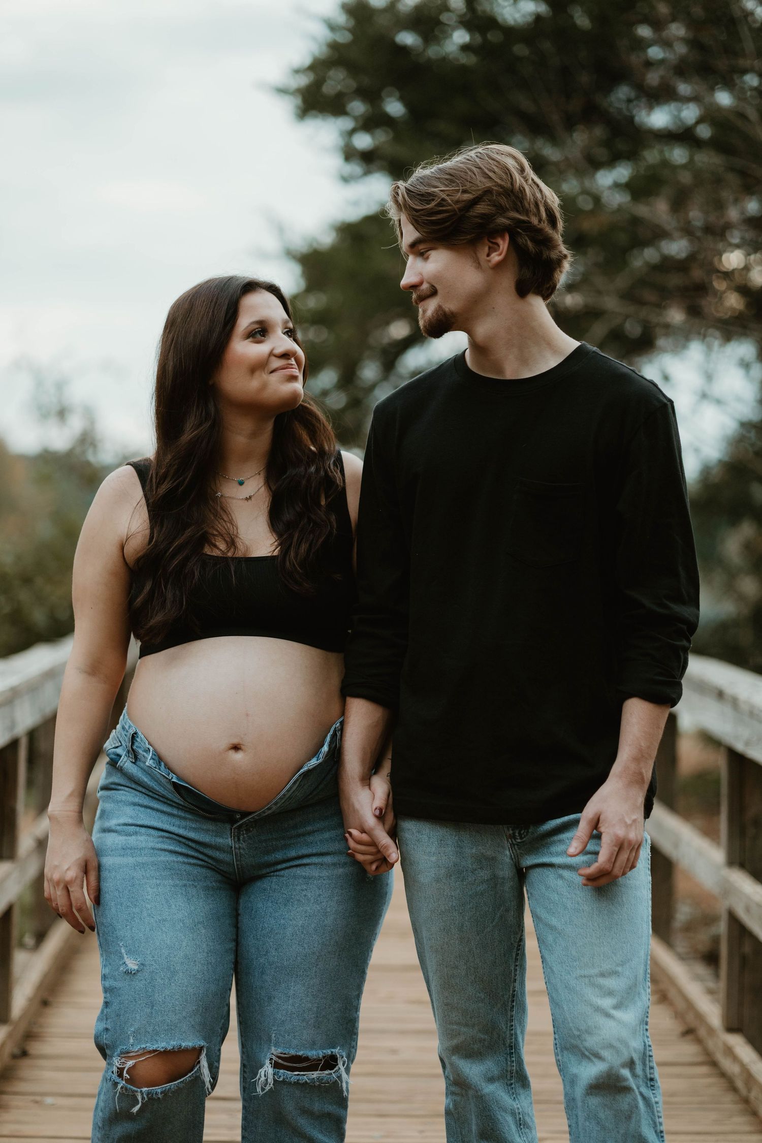 A couple on a wooden walkway in matching outfits sharing romantic moments during a maternity photo shoot.
