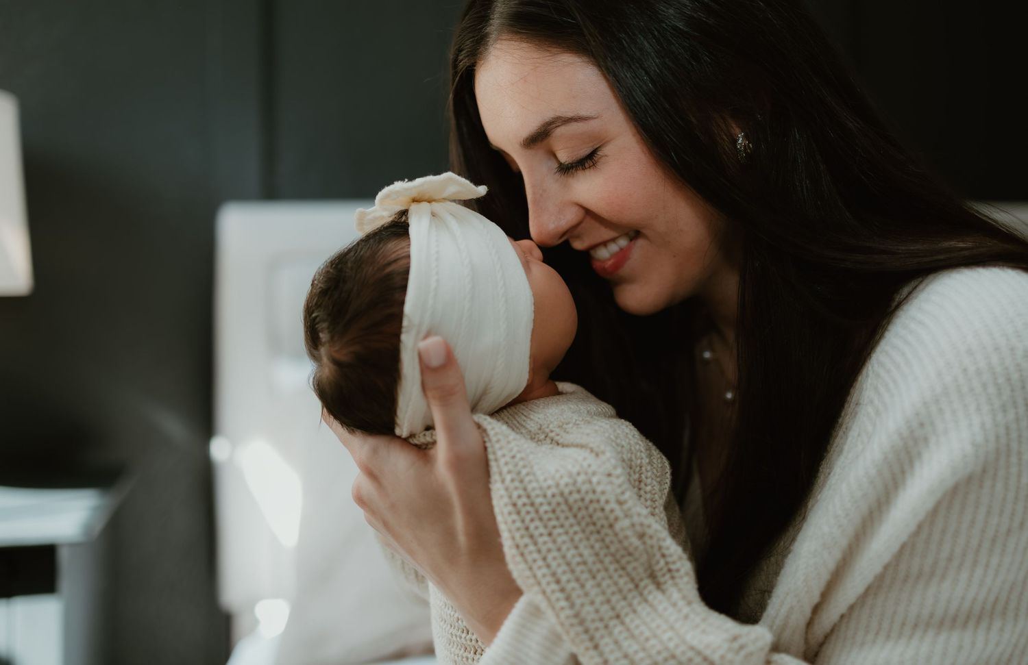 A tender moment between parent and baby both wearing white sweaters in cozy intimate lighting.