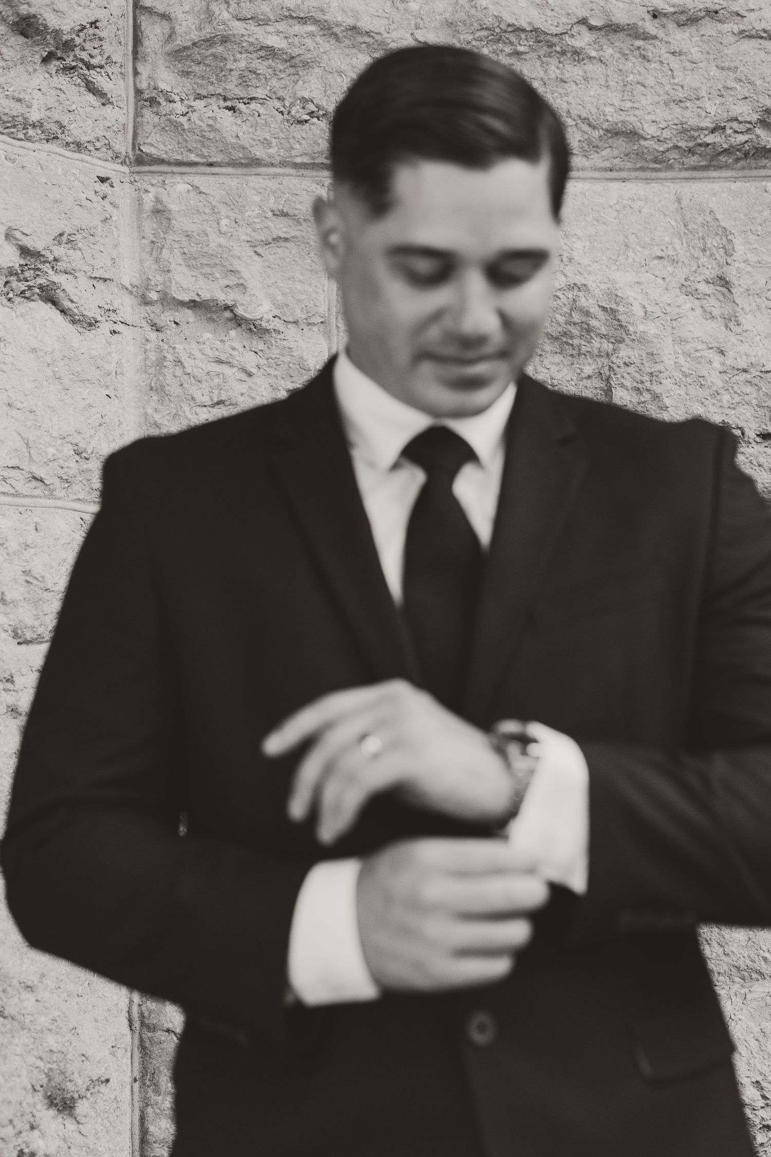 Person in dark suit adjusts their cuff in a sequence of black and white photographs against a stone wall.