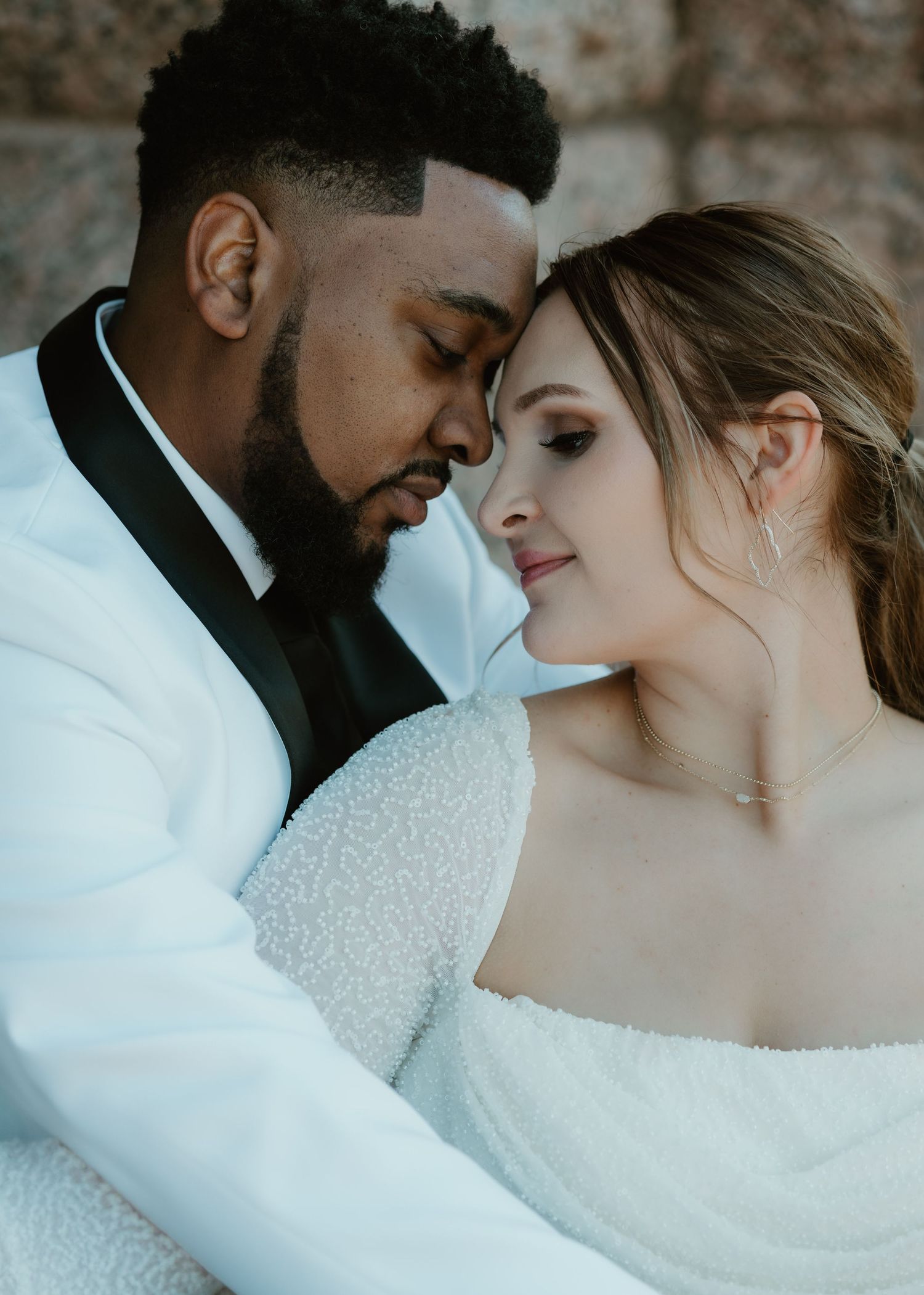 A romantic wedding portrait shows a couple in white attire sharing an intimate close-up moment against a blurred background.