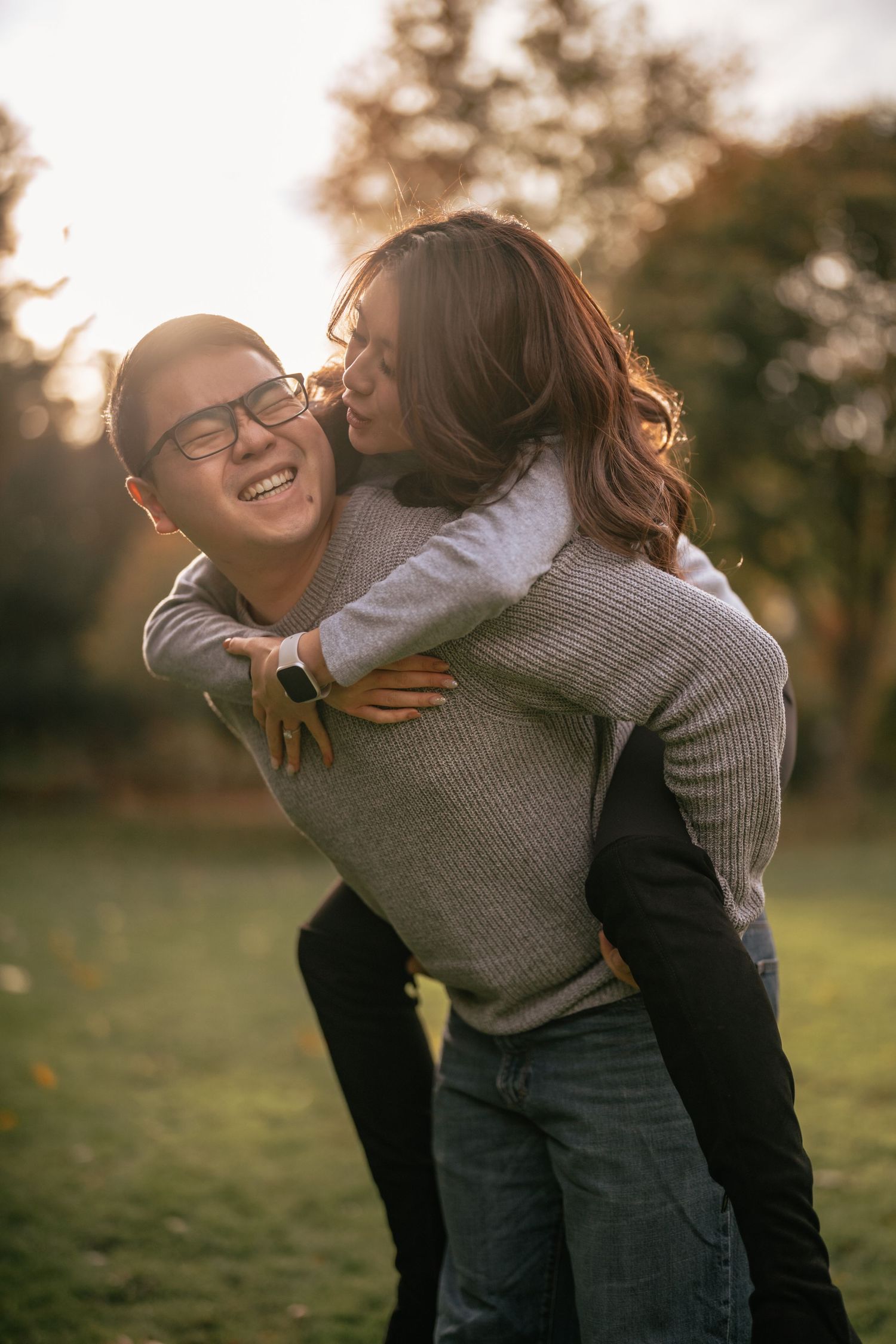 Two people sharing a joyful piggyback ride moment outdoors at sunset with warm backlighting in a park setting.