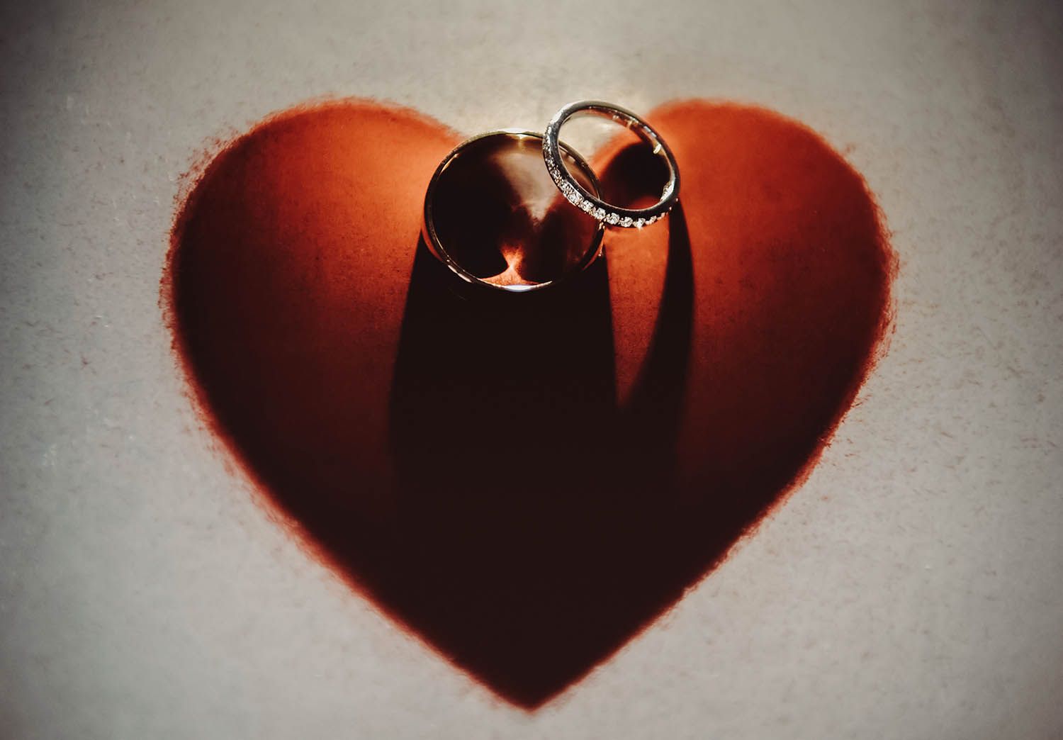 Two wedding rings cast a shadow on a red heart-shaped background in a romantic silhouette.