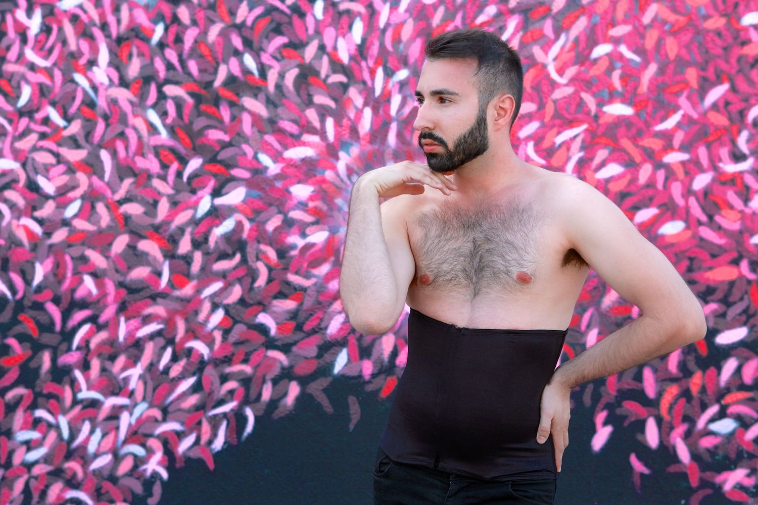 Artistic portrait against pink graffiti wall features shirtless person in black top striking contemplative pose in a miami portrait shoot