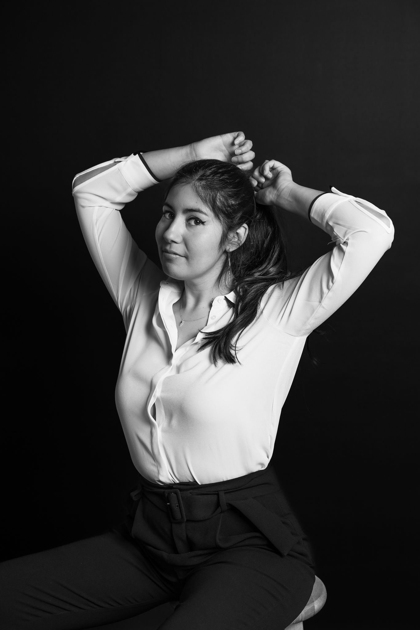 Woman in white button-down shirt poses dramatically against dark background in monochrome portrait in a miami portrait photography shoot