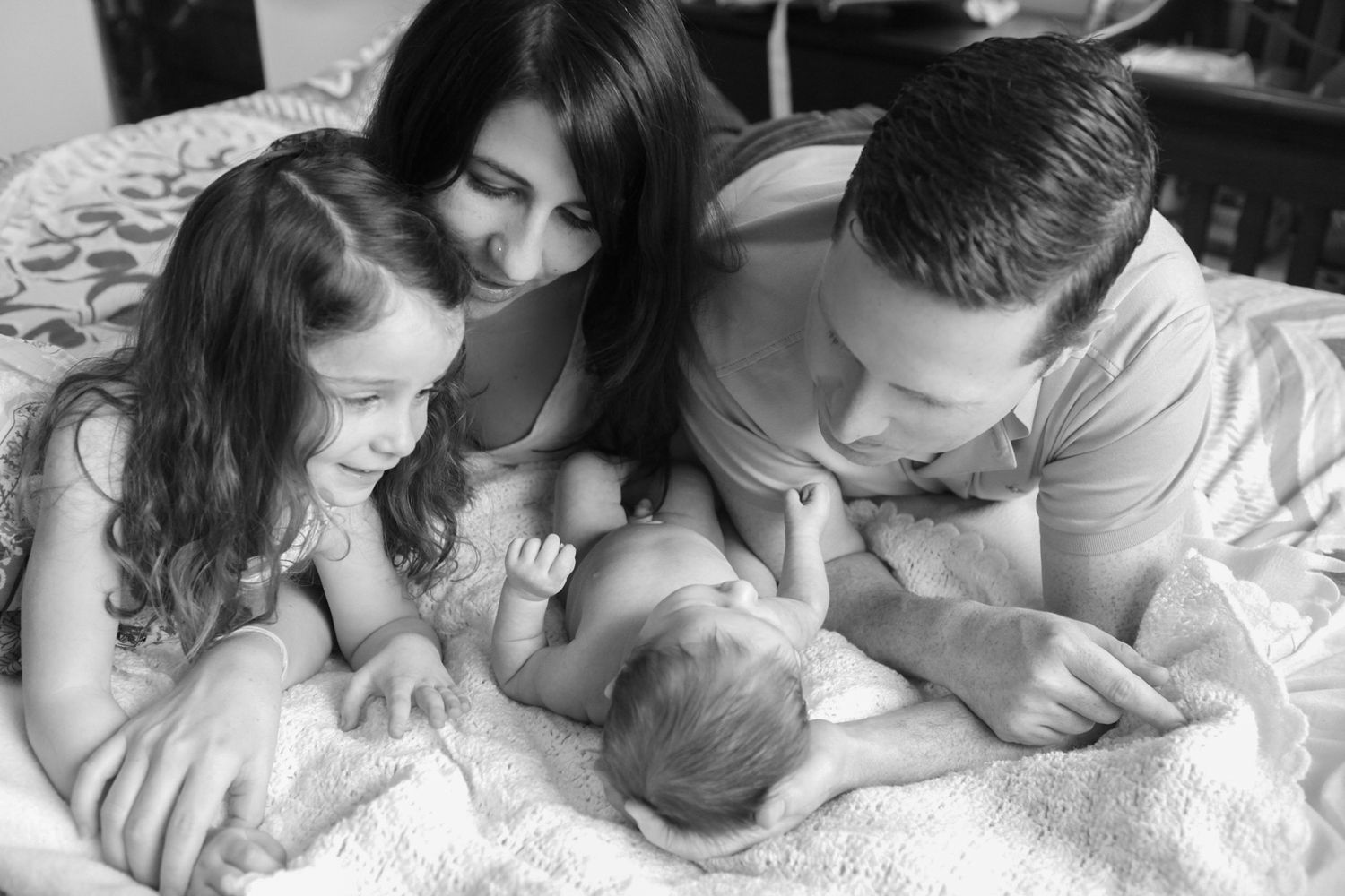 A tender black and white moment as a family welcomes their newest member on a bed in a lifestyle family portraits shoot in miami