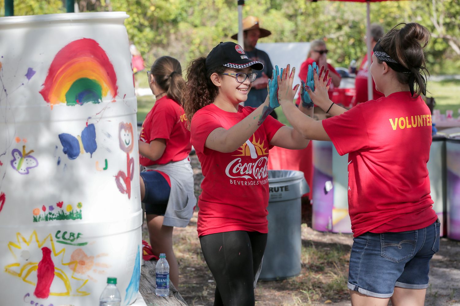 Community volunteers in red shirts participate in outdoor art project with colorful mural elements for an Event Photography in Miami