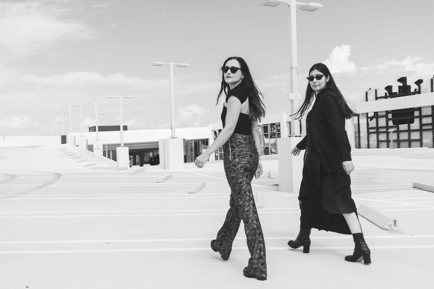 Four black and white fashion photos show people walking through an urban setting with minimalist architecture.
