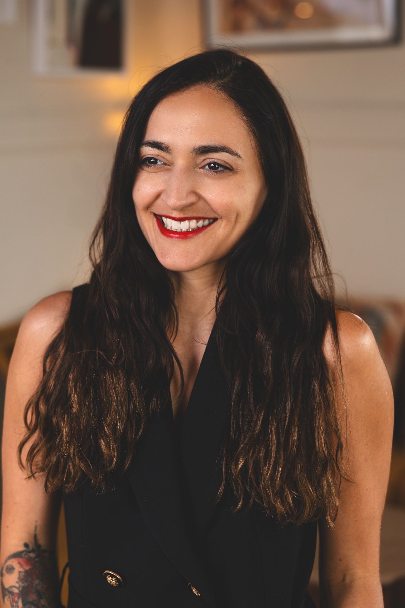 A collage showing four smiling portraits of someone with dark wavy hair and bright red lipstick against a blurred background.