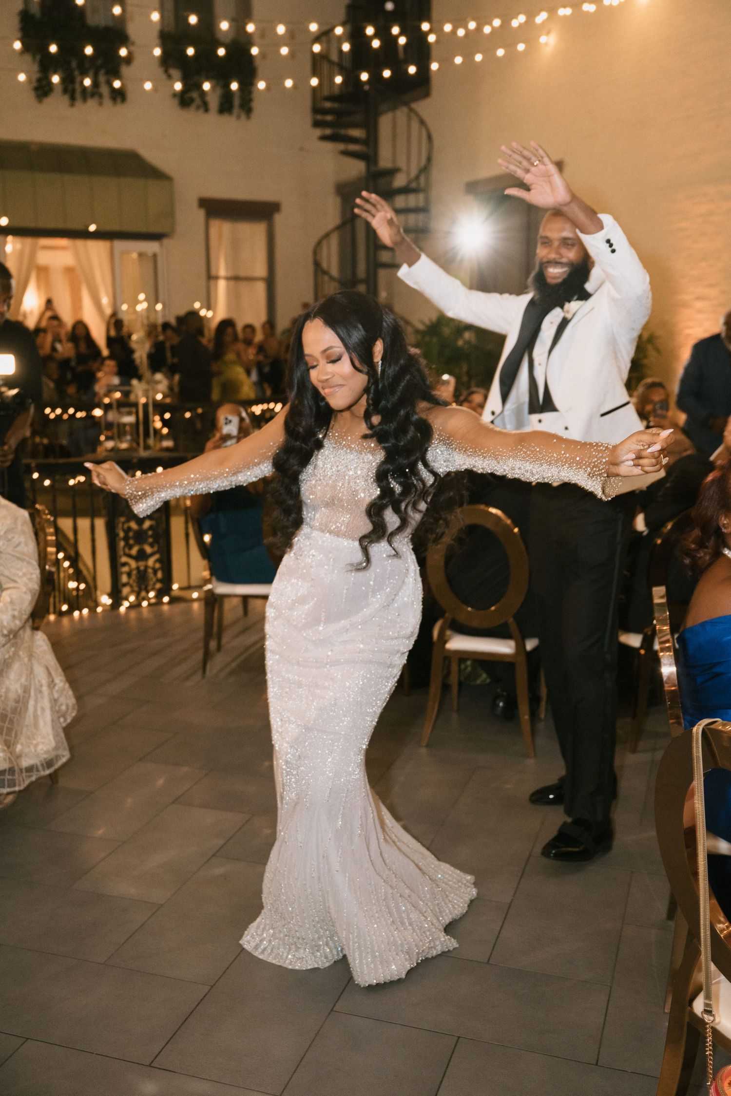 Wedding reception scene with guests dancing under string lights in an elegant venue.
