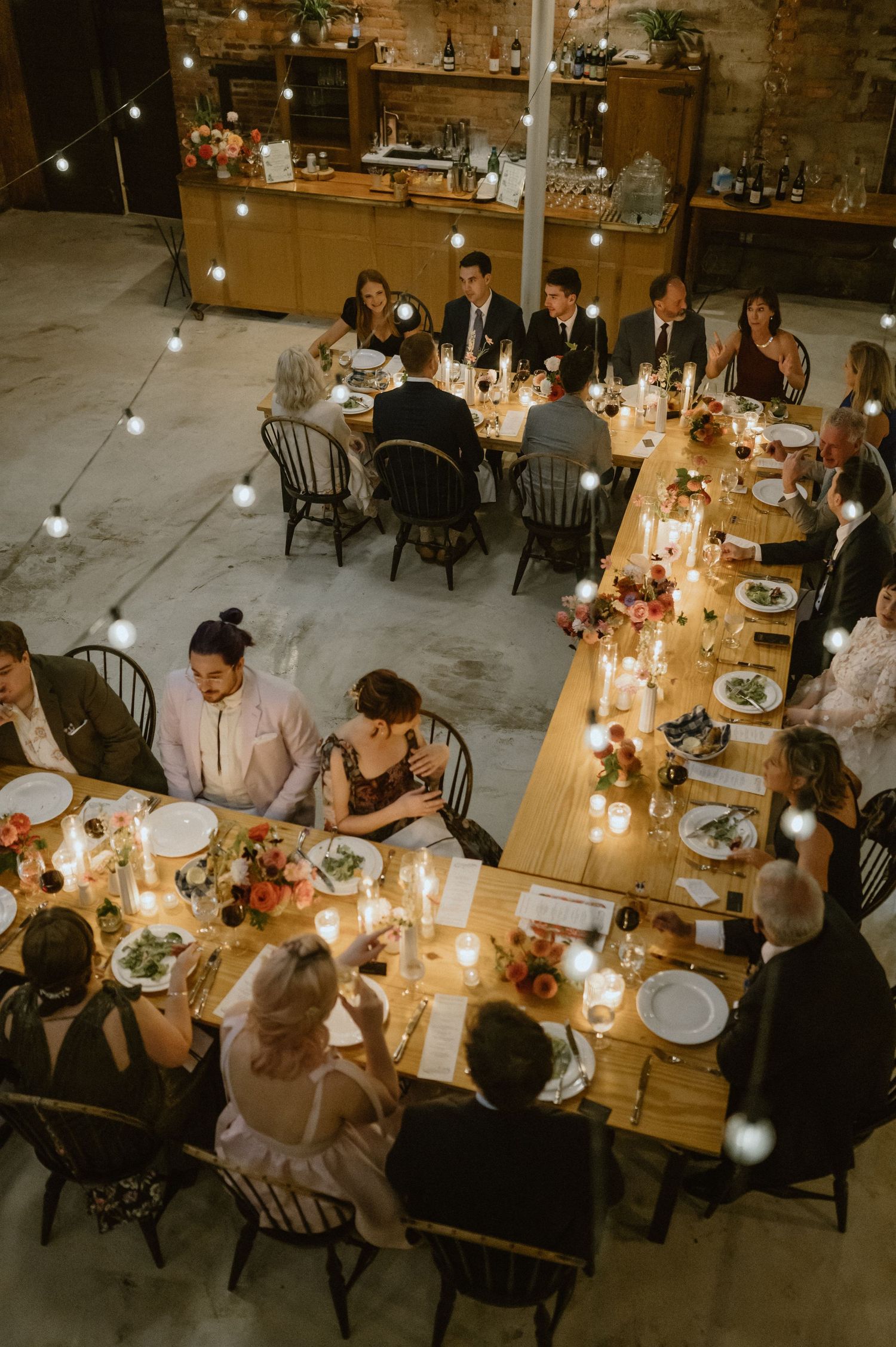 Intimate wedding reception dinner with warm lighting and rustic wooden tables in an industrial venue.