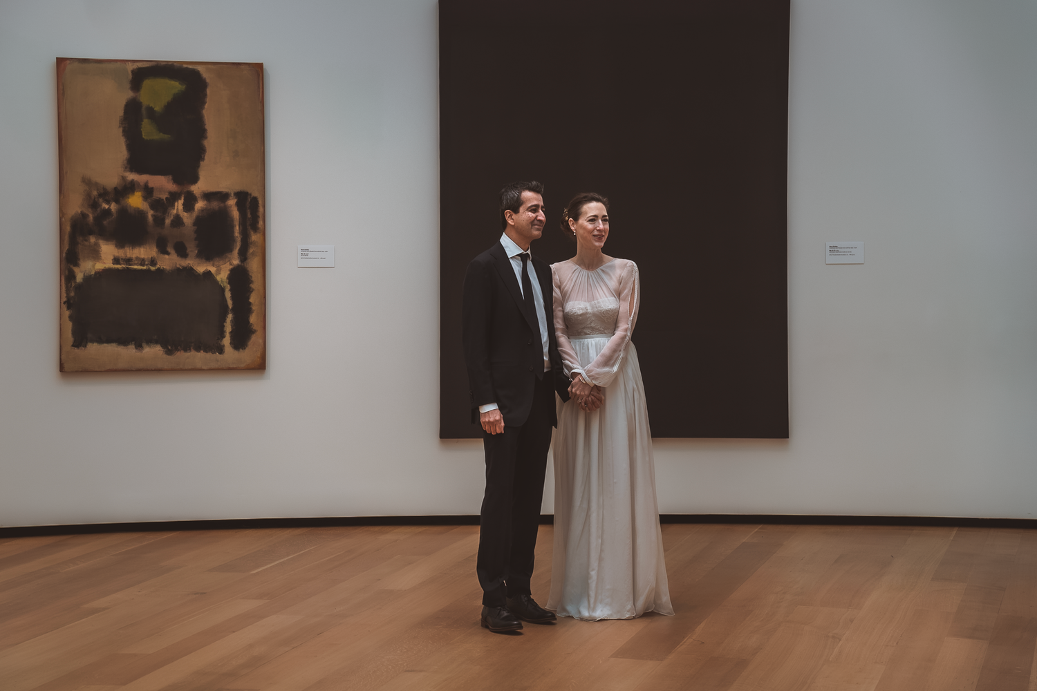 Couple in wedding attire standing in an art gallery with modern paintings on display.
