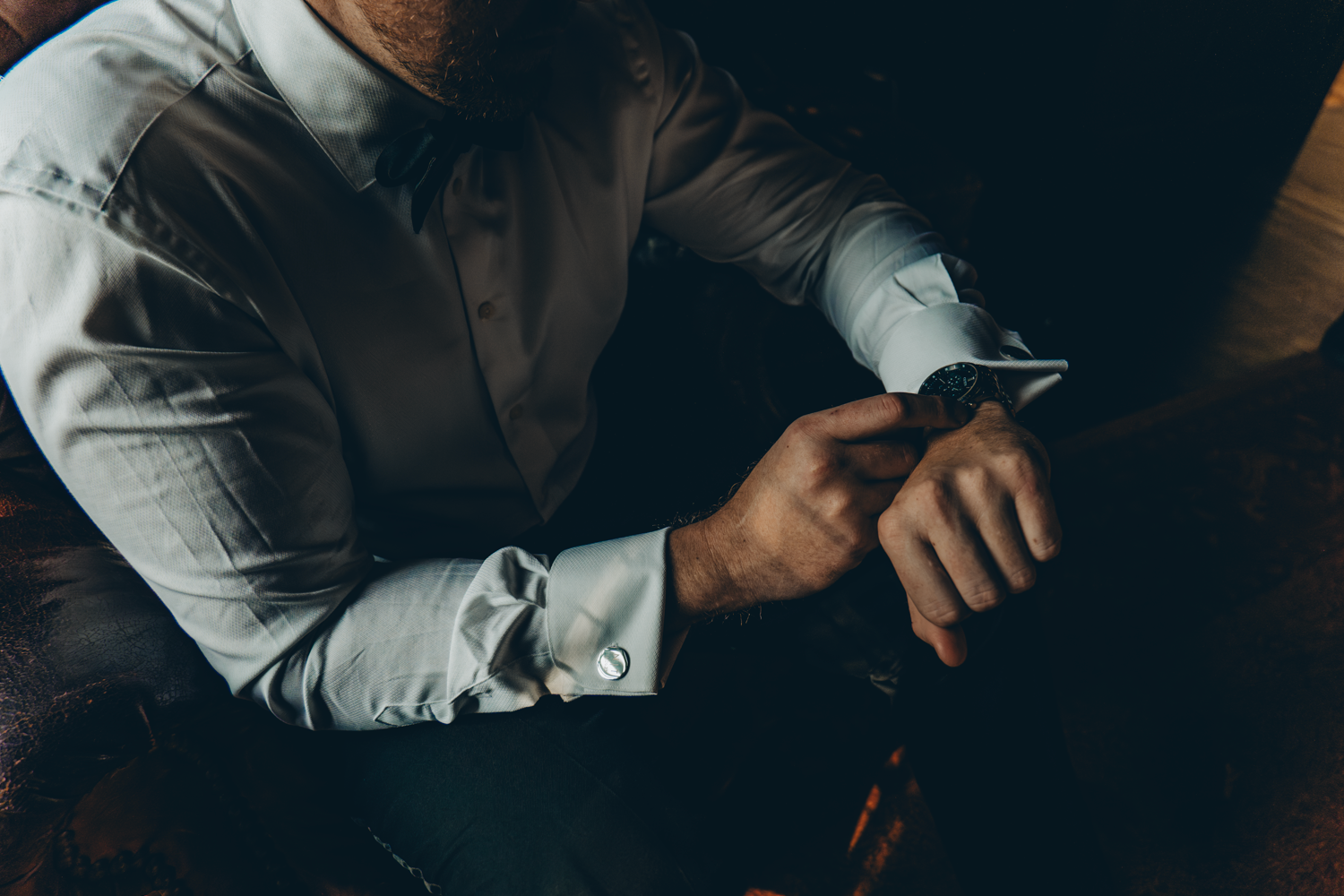 Person in white dress shirt checking smartwatch in dark lighting conditions.