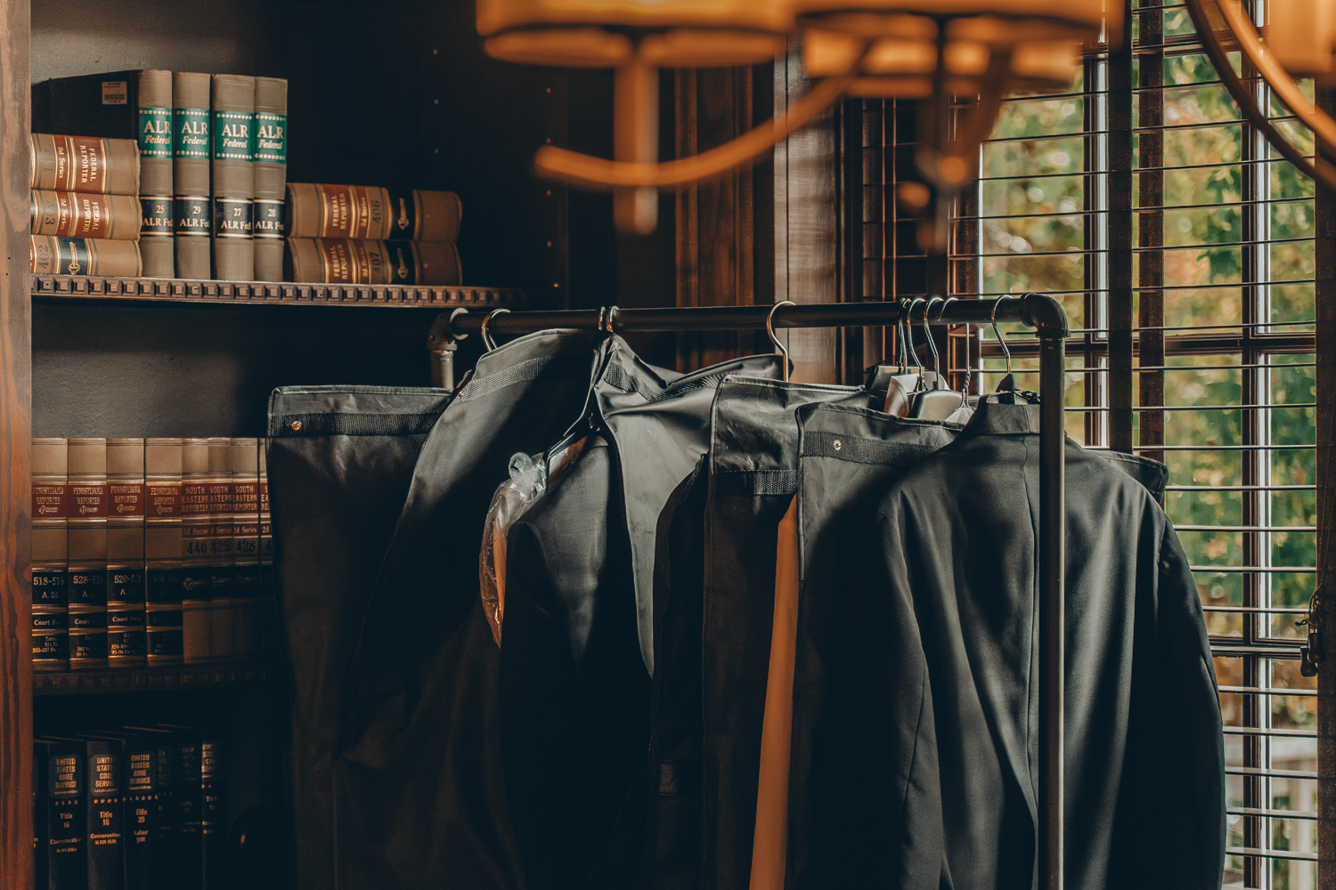 Row of black leather jackets hanging on clothing rack in a dark rustic retail space with warm lighting.