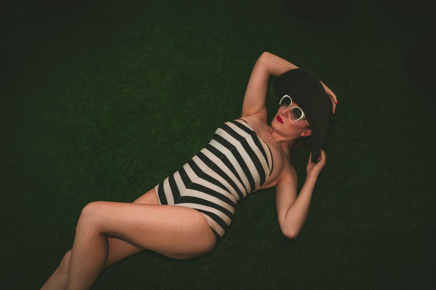 A person in a black and white striped swimsuit poses artistically against a dark green background.