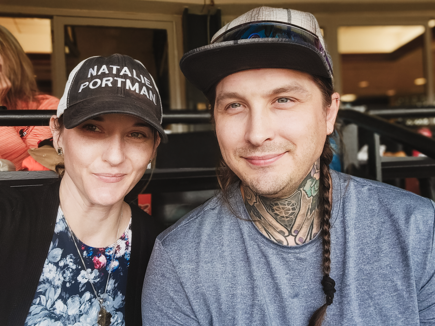 Two people wearing casual attire sit together smiling at the camera in what appears to be a restaurant setting.