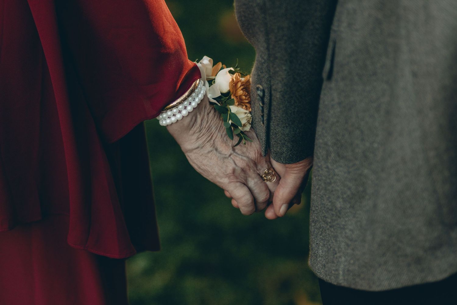 Two hands lovingly clasped together, wearing elegant bracelets and delicate floral wrist corsages.