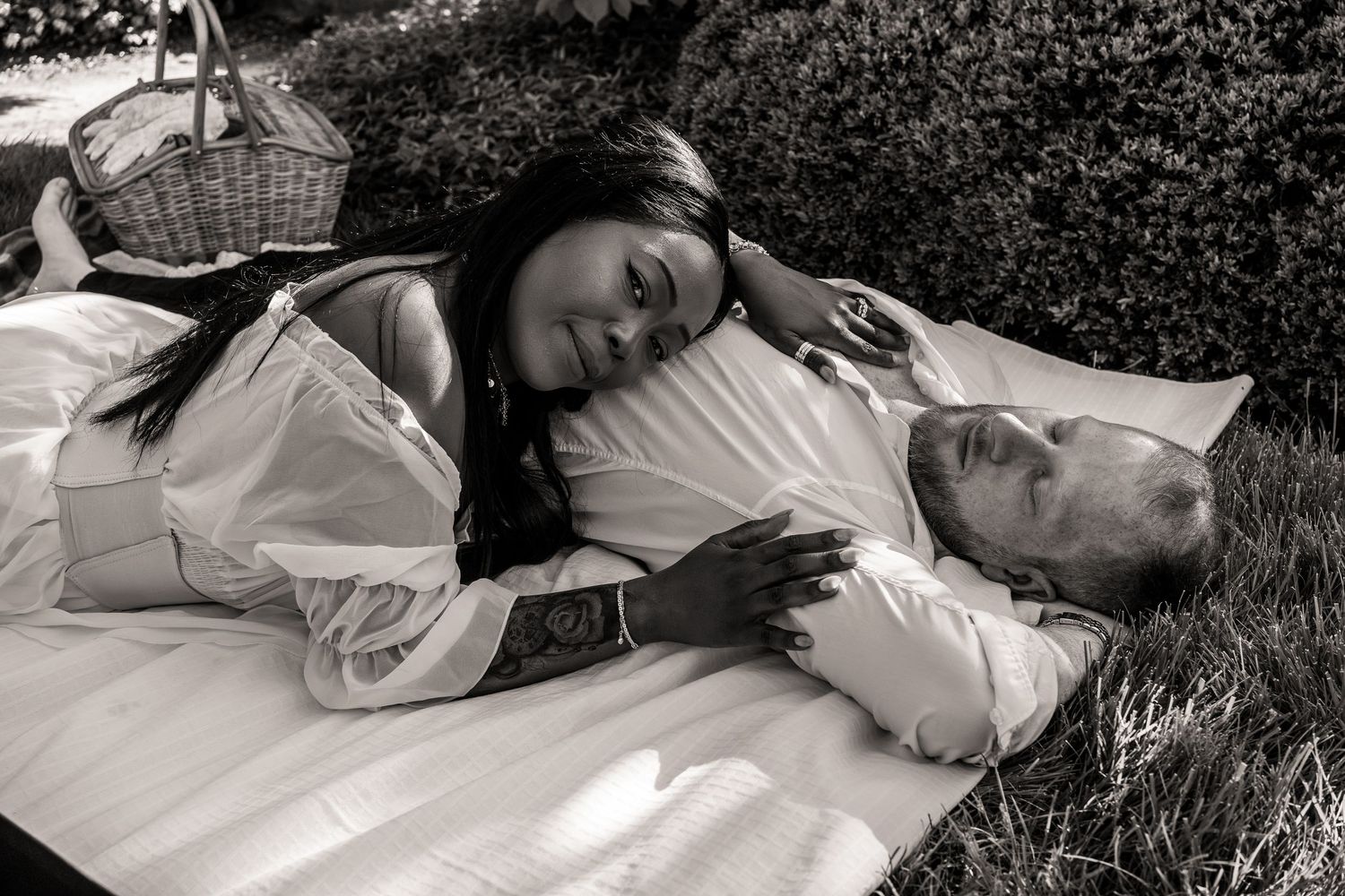 A couple lying together on a picnic blanket in black and white, with a basket visible nearby.