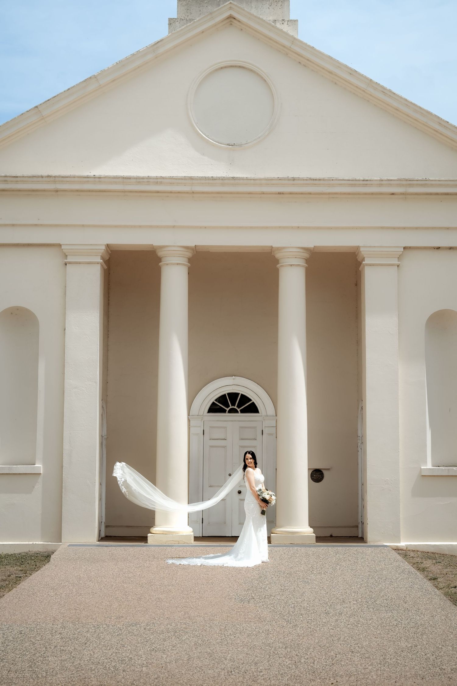 Classic white chapel wedding venue with elegant columns and a flowing bridal veil in the breeze.