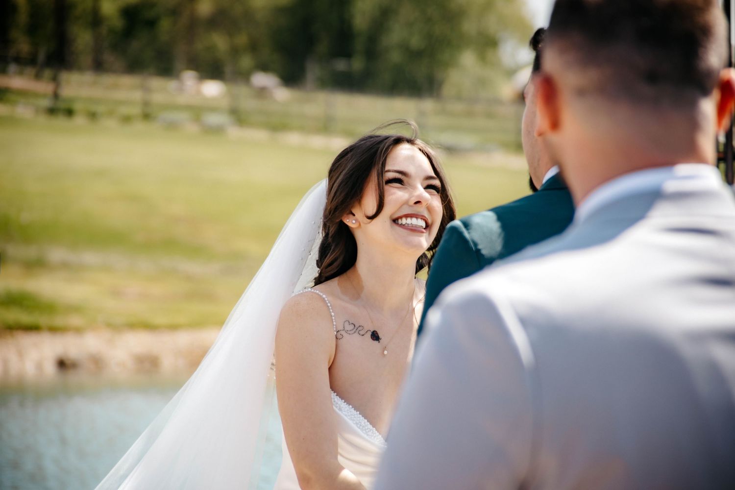 Happy couple shares a joyful moment by a lake during their outdoor wedding ceremony.