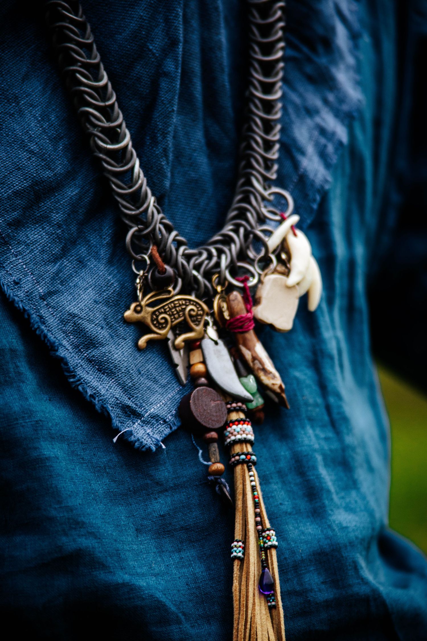 Closeup of a bohemian charm necklace with vintage trinkets and tassels against blue denim fabric.