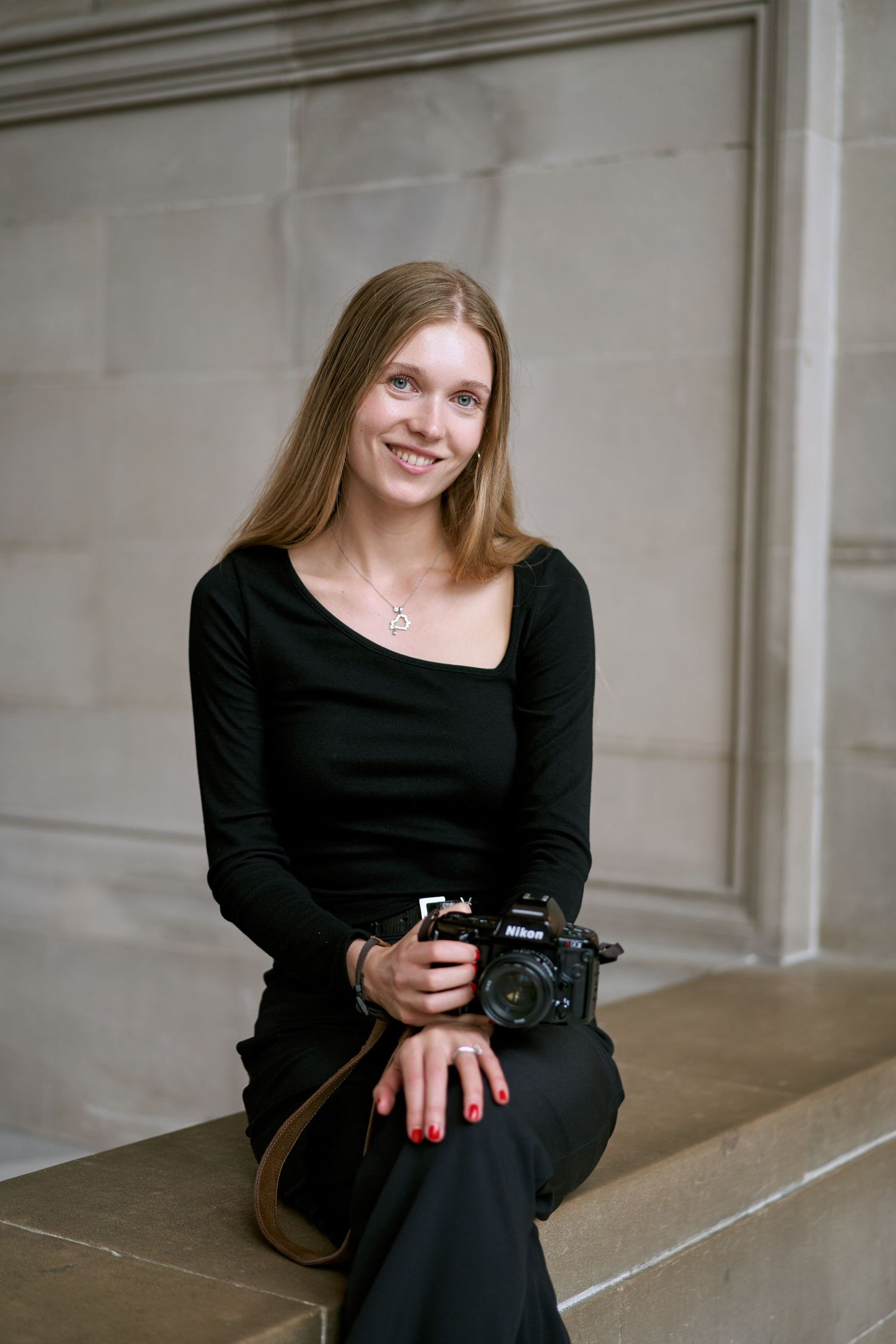 A photographer in a black outfit sits on stone steps while holding a professional camera.