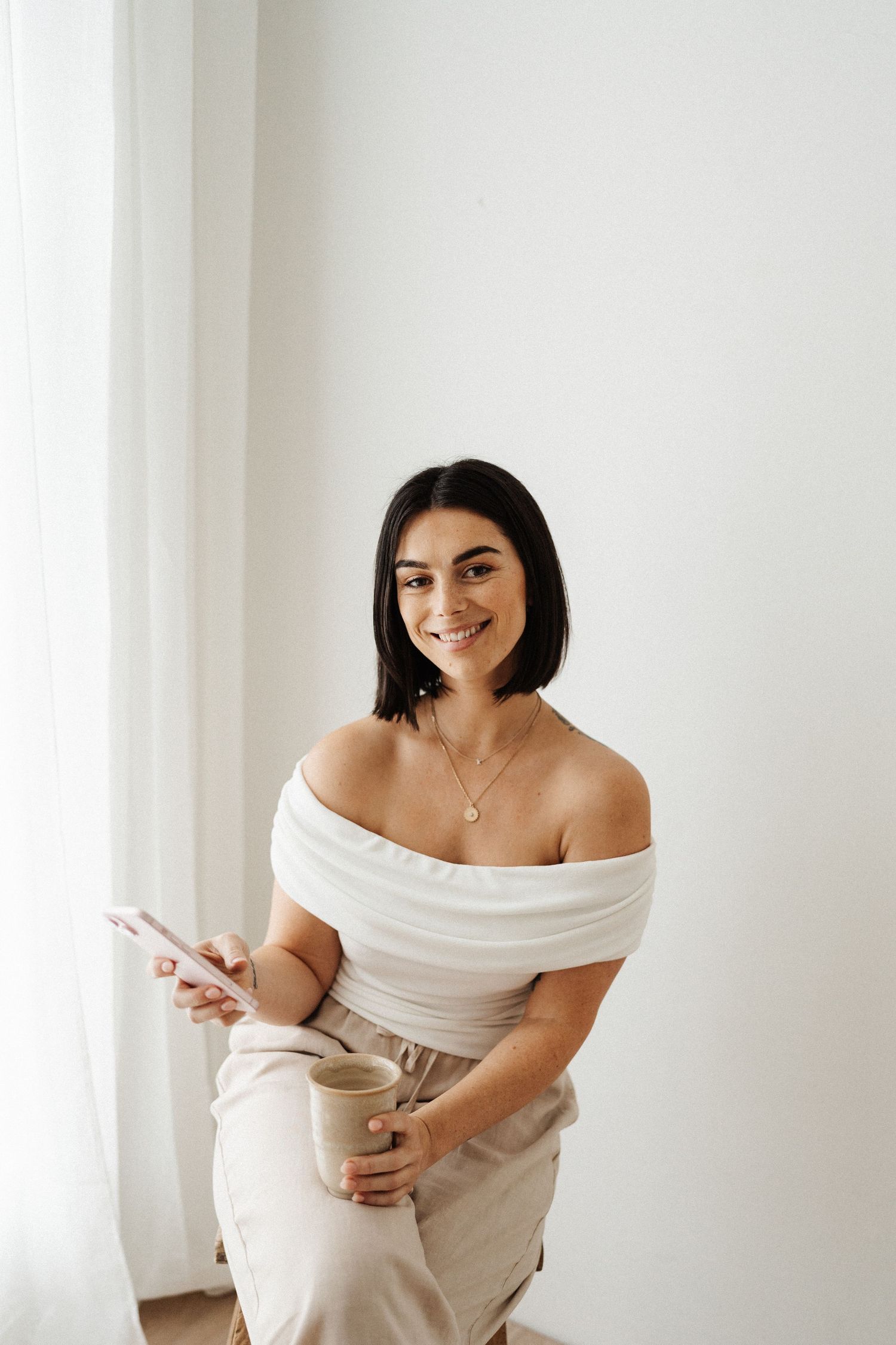Portrait of someone in an off-shoulder white top and beige skirt against a light wall.
