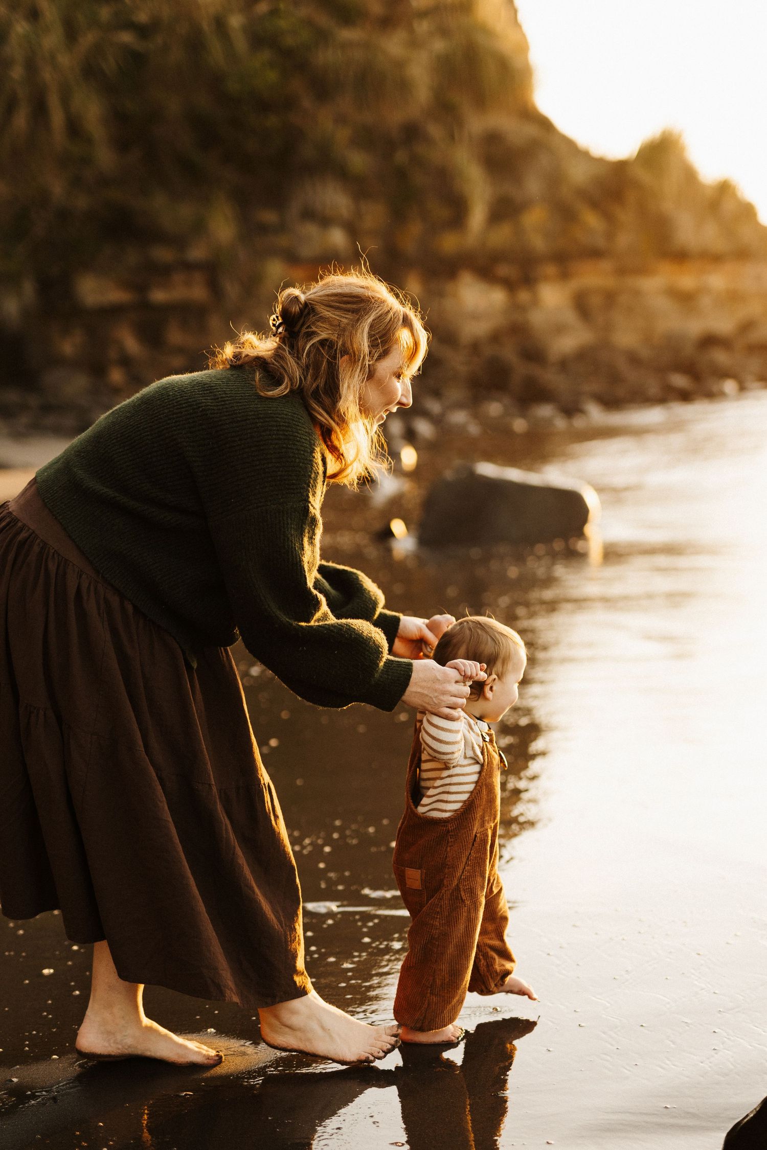 A figure sits on a rocky beach at sunset, creating a warm and moody silhouette against the golden light.