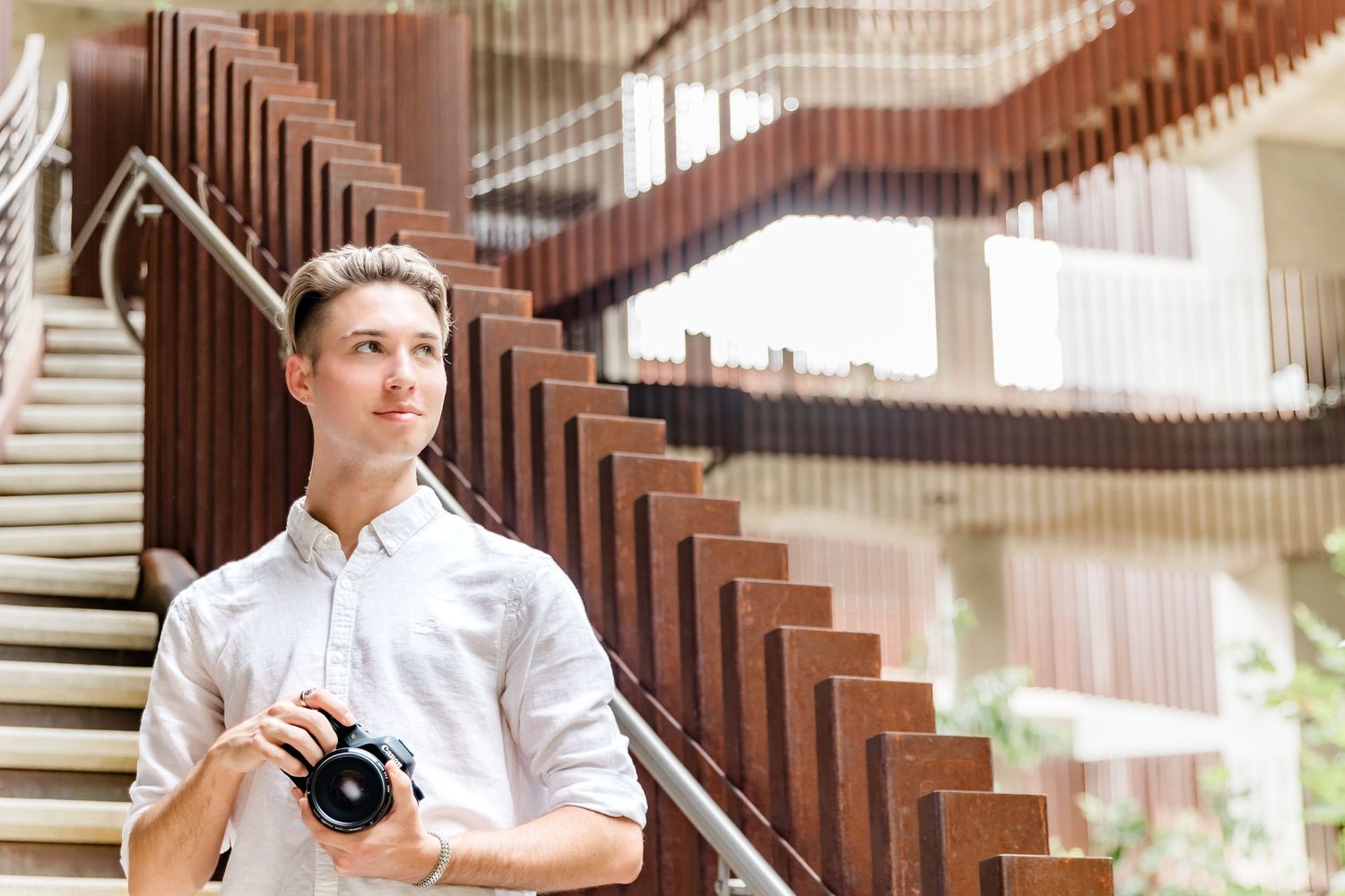 Person standing near modern wooden staircase holding camera indoors.