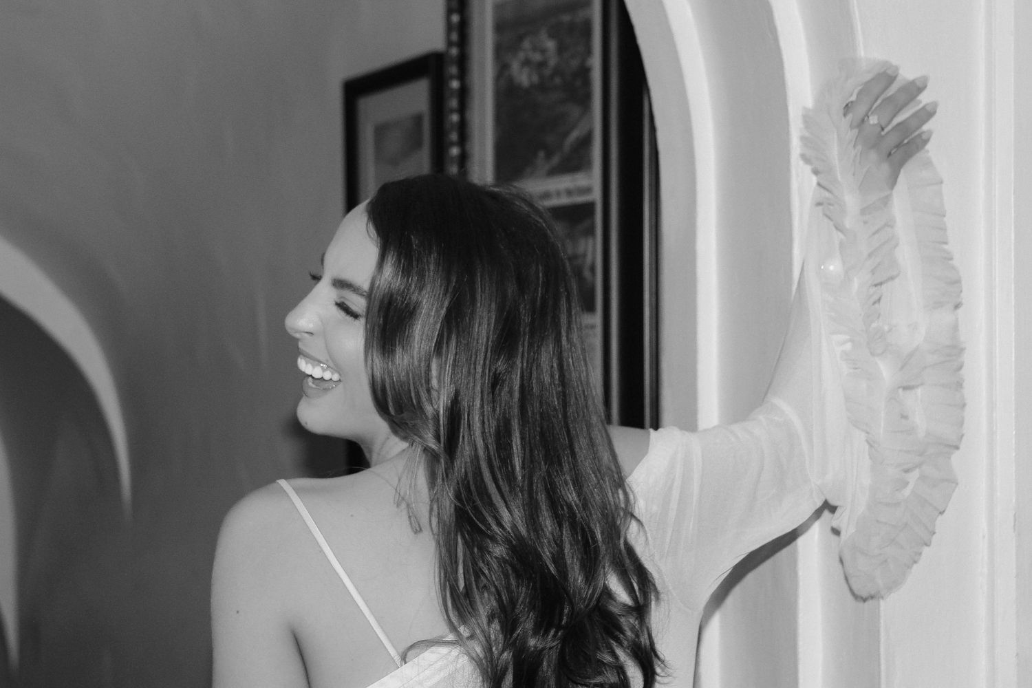 Black and white portrait of someone in white dress looking to the side near wall.