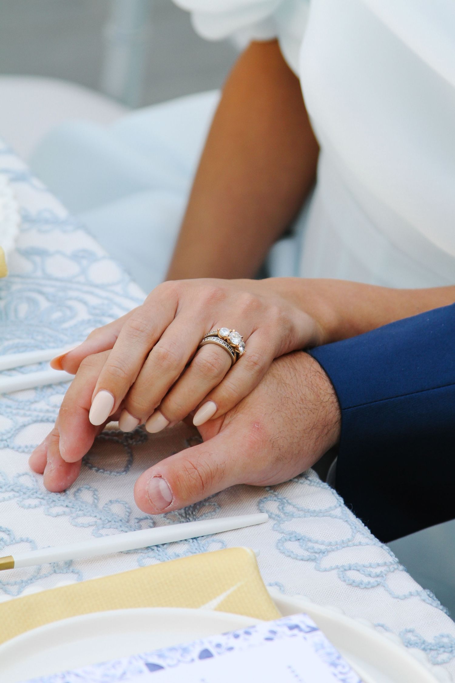 Close-up of newlywed couple's hands with wedding rings resting on a tablecloth.
