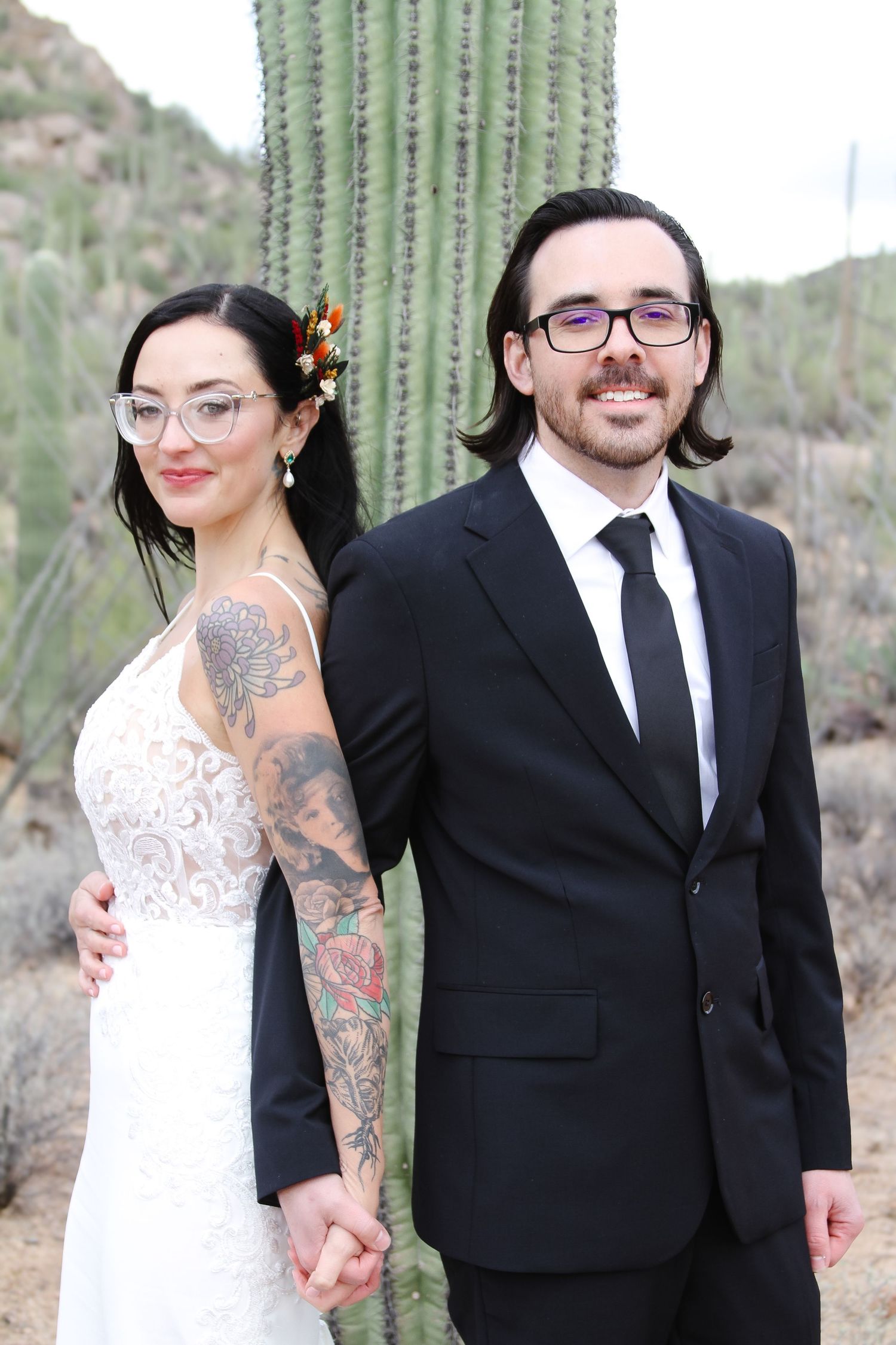 Wedding couple posing together near a large saguaro cactus in the desert.