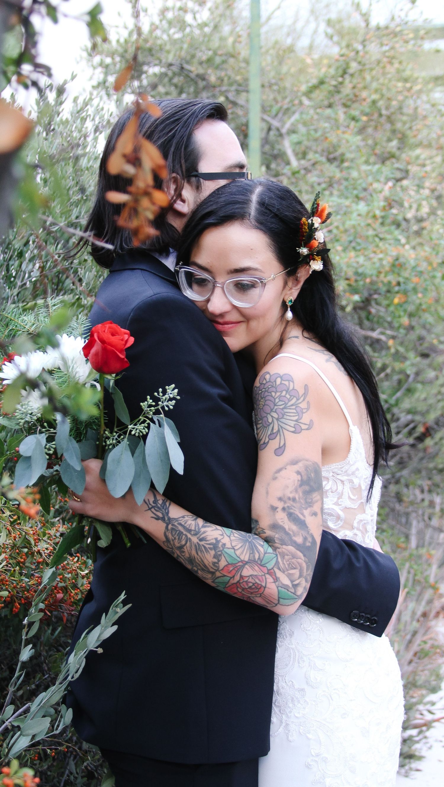 Two people embrace at a wedding with one wearing a lace dress and floral accessories.