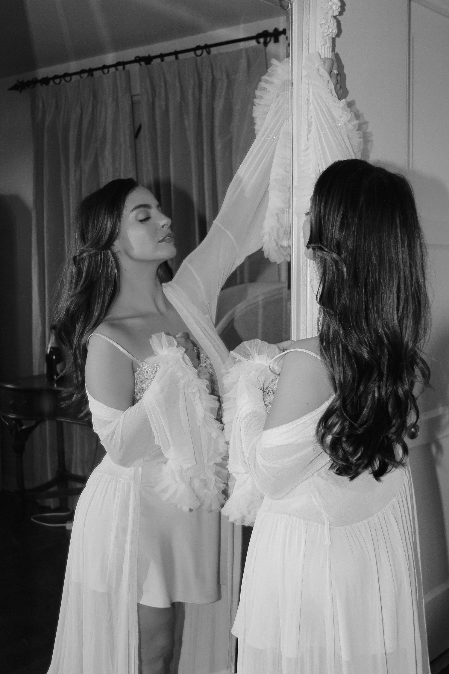 Two people examining white formal dress hanging on display in room.