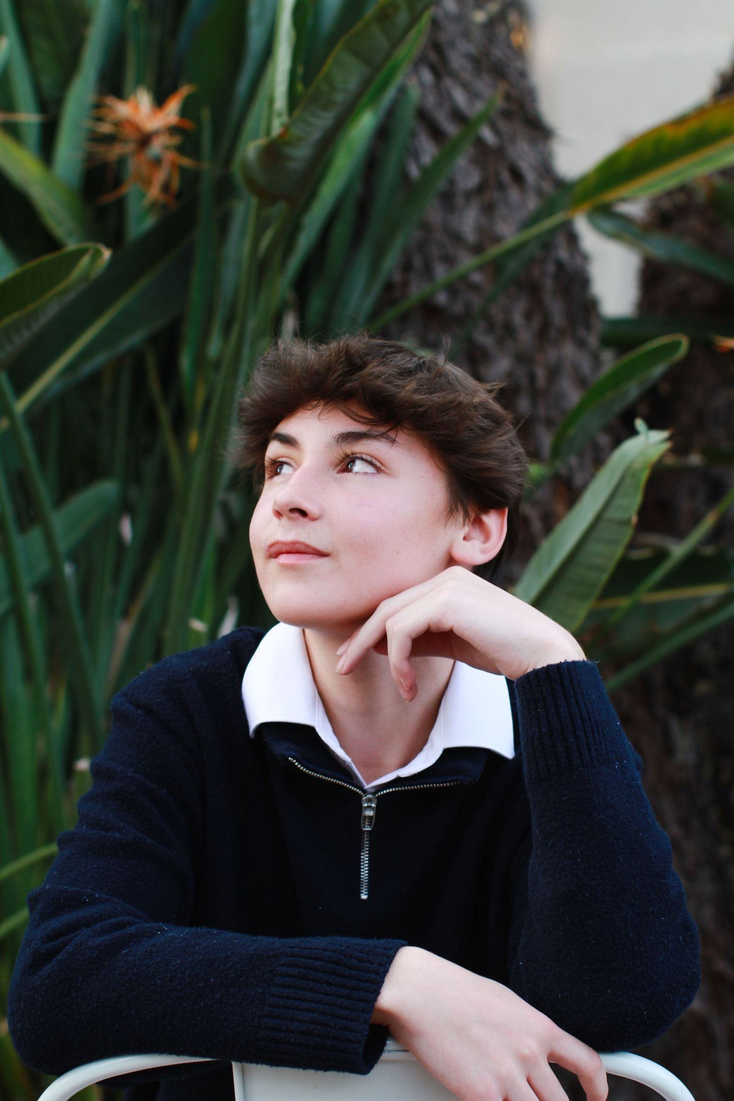 Portrait of person in navy sweater looking thoughtfully away near tropical plants.