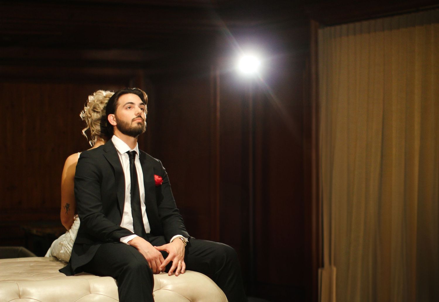 A stylish wedding portrait with dramatic lighting showing a seated couple in formal attire.