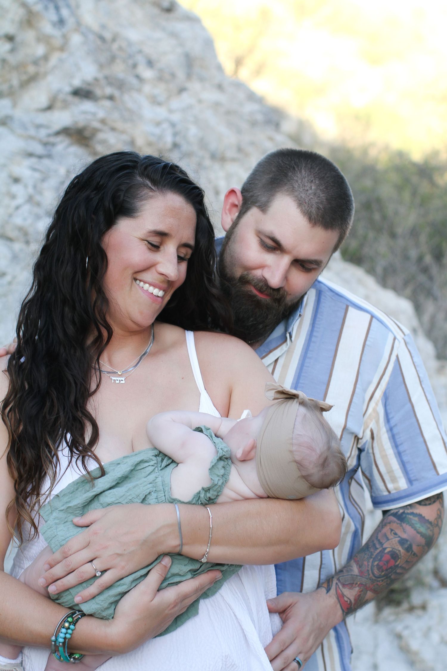 A family shares an intimate nursing moment together against a rocky outdoor backdrop.