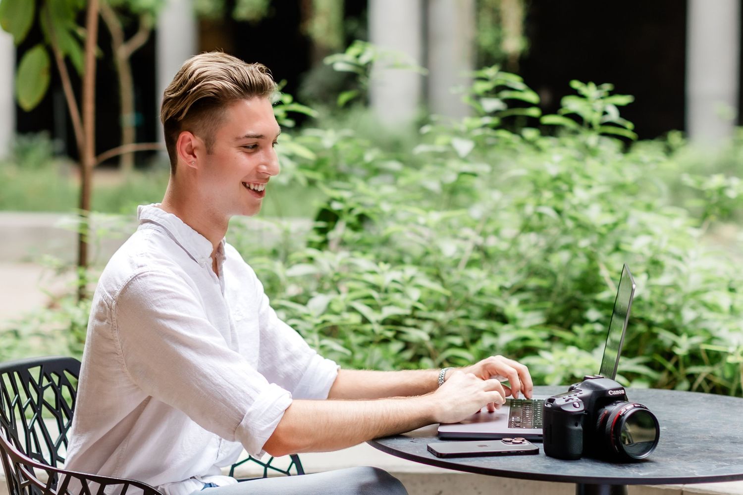 Someone working on laptop at outdoor patio table surrounded by greenery.