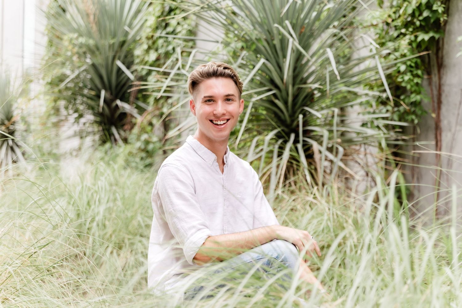 Person in white shirt smiling while seated in garden setting with tropical plants.