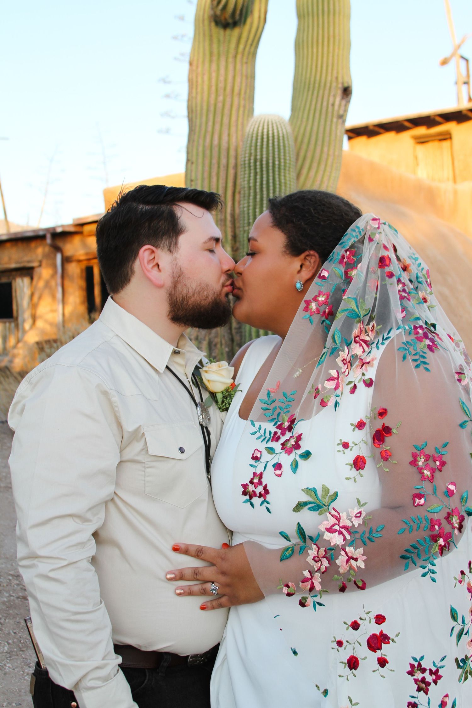 Couple sharing tender moment against desert landscape with flowering cactus.