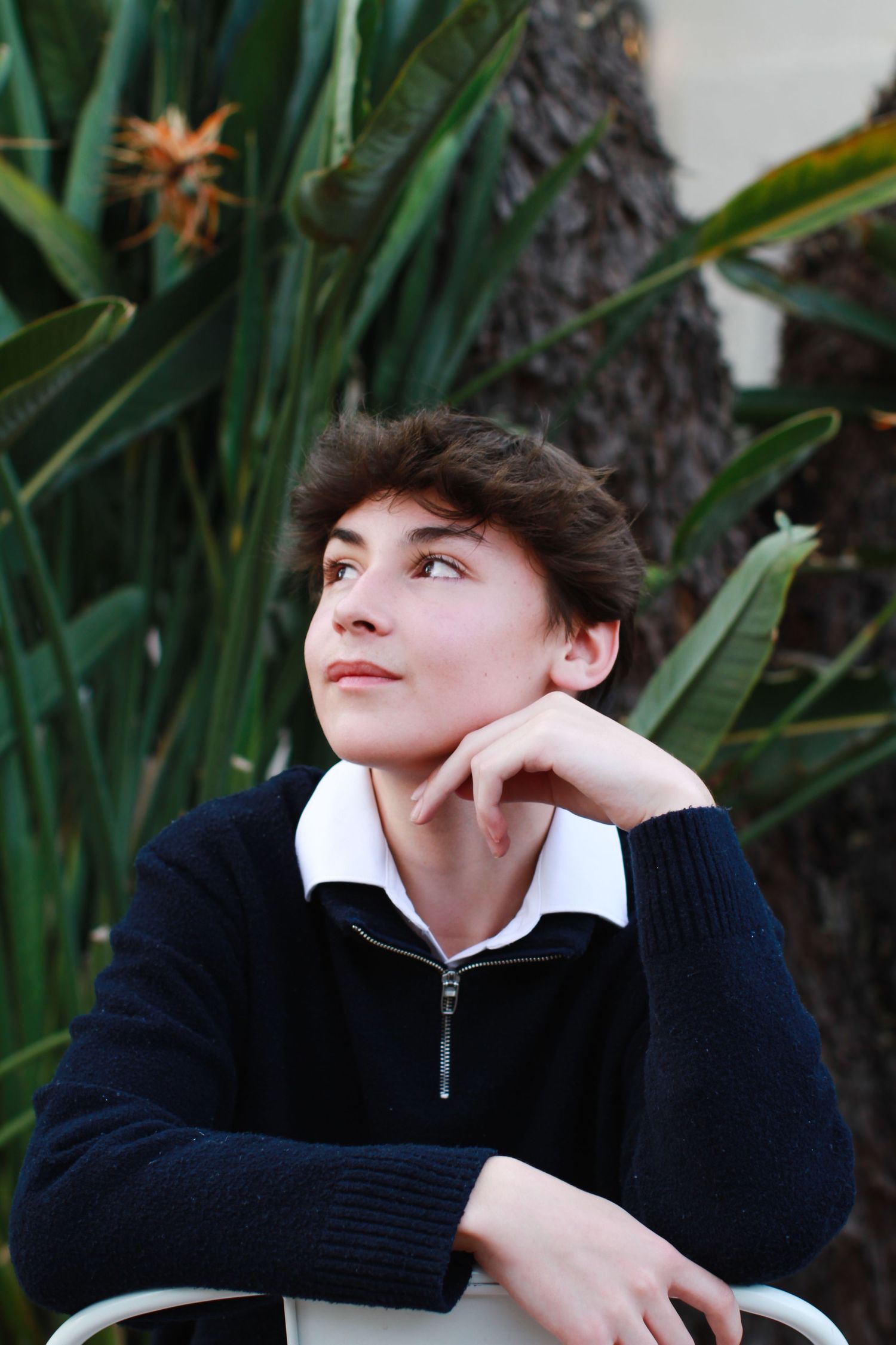 Thoughtful portrait of person in navy sweater posed against tropical foliage background.