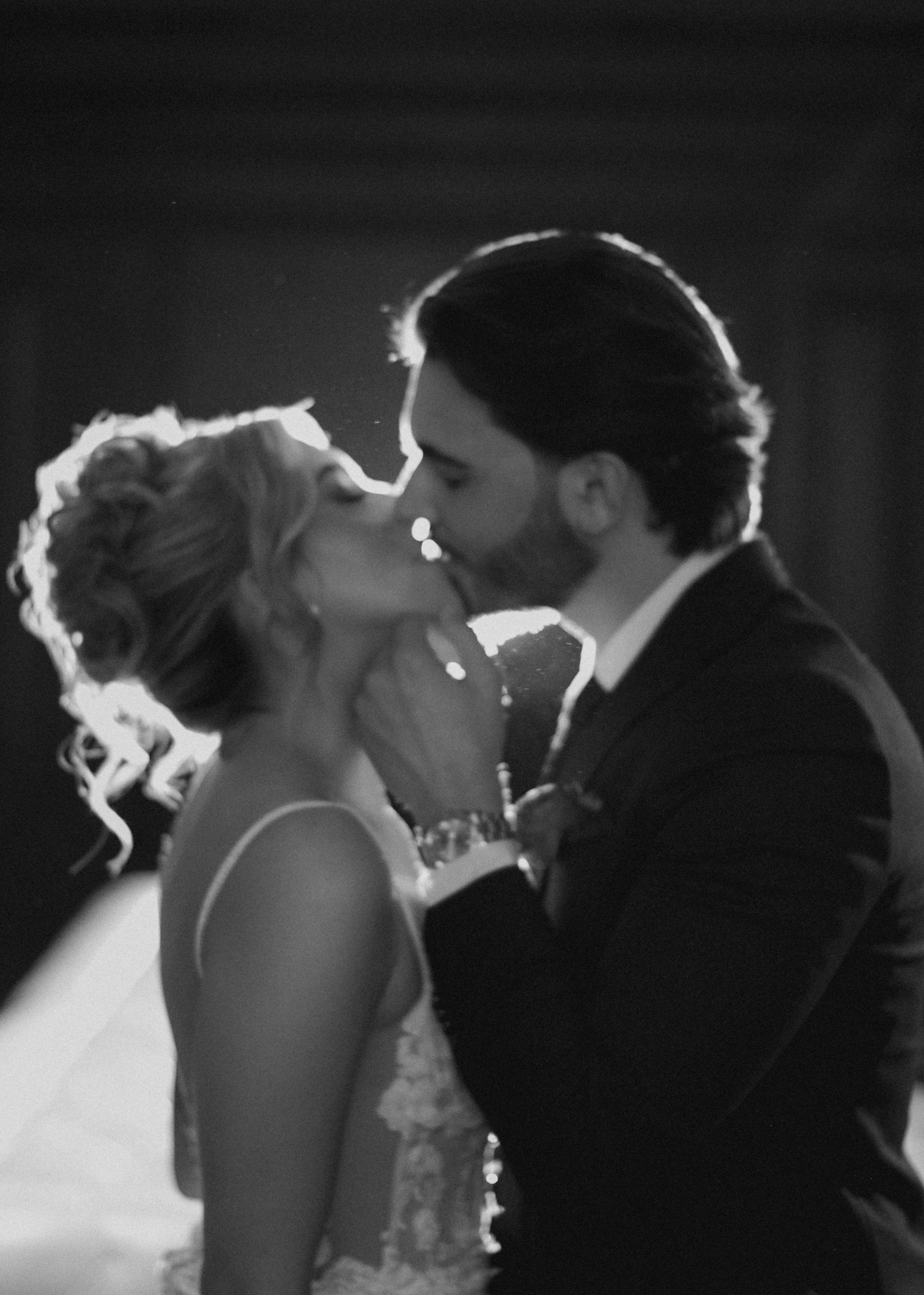 Intimate black and white portrait of newlywed couple sharing their first kiss.