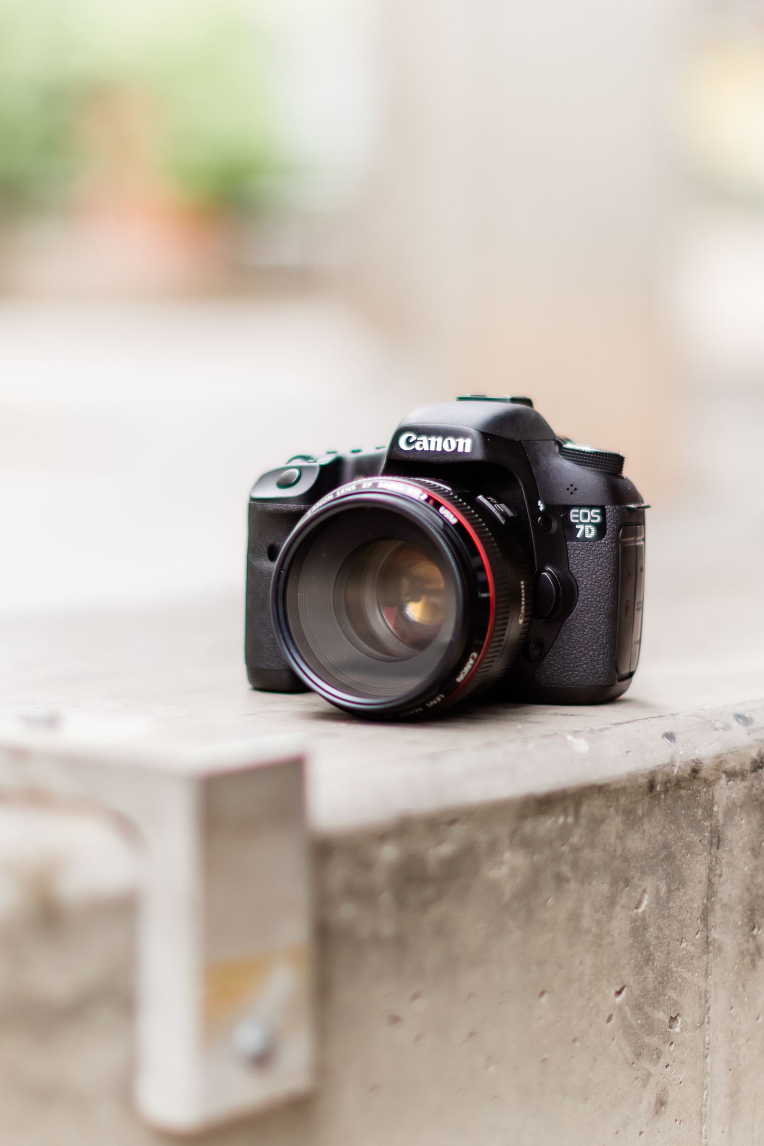 Canon 7D DSLR camera with telephoto lens sitting on concrete ledge.