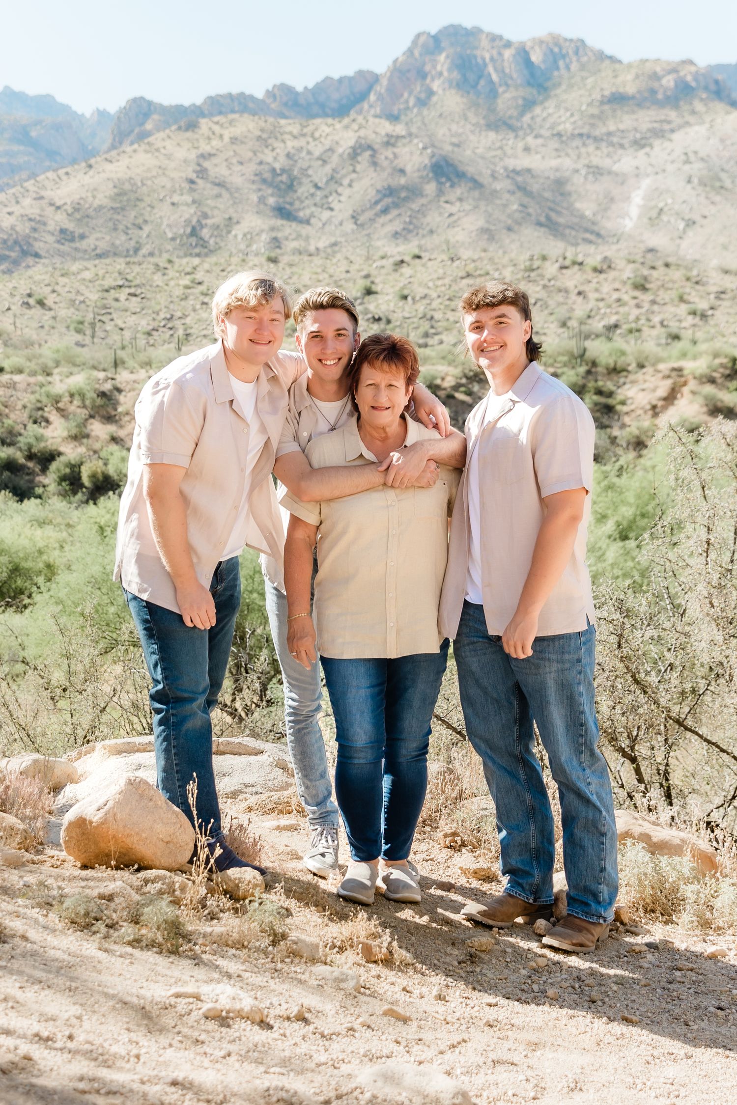 Family portrait of four people standing together on desert trail with mountains behind.