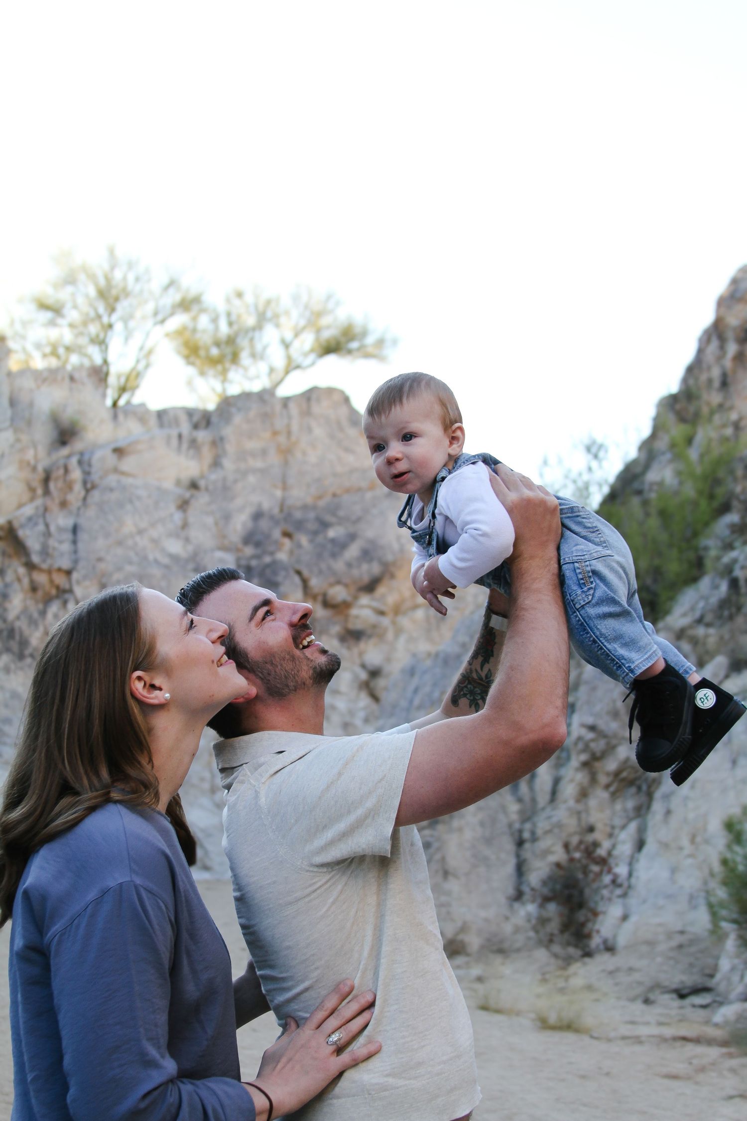 Happy family moment with baby being lifted high against desert cliff backdrop.